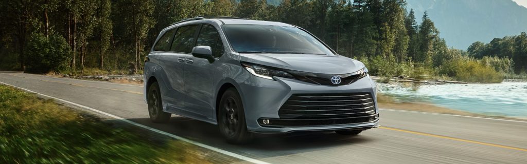 2026 Toyota Sienna minivan driving along a scenic forest road beside a river, highlighting its family-friendly design and smooth performance.
