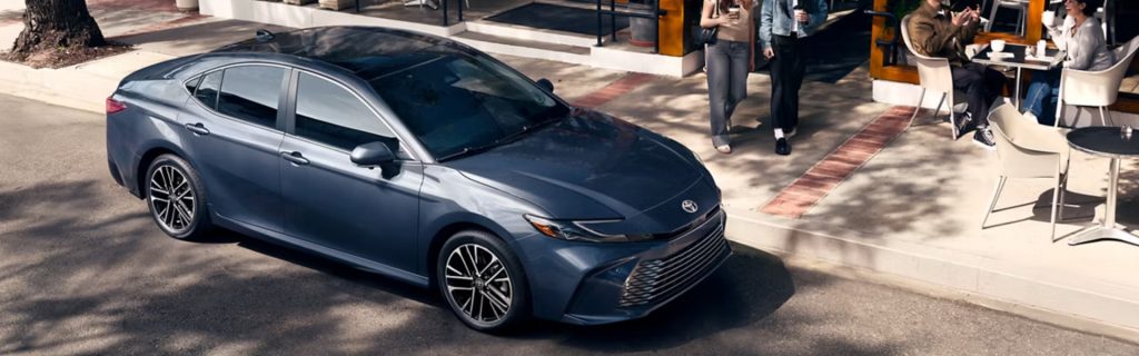 2026 Toyota Camry in sleek blue, parked by a café, highlighting its stylish and sporty design.
