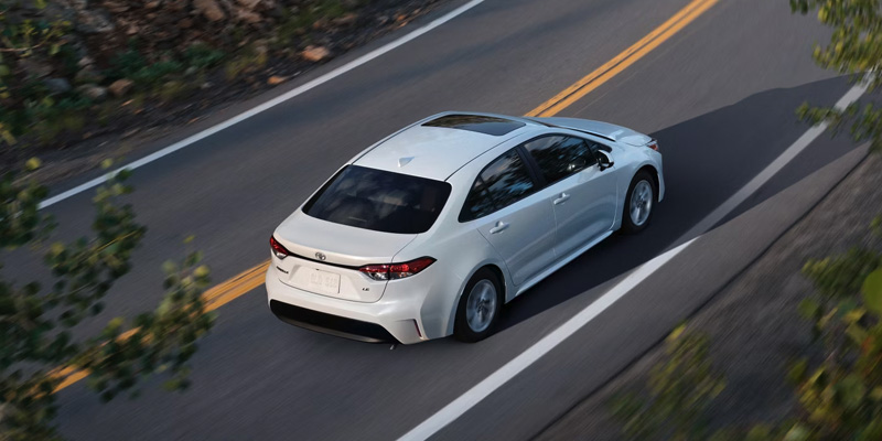 2026 White Corolla Hybrid cruising on road in its stunning back profile