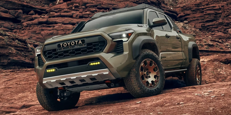 Toyota Tacoma pickup truck navigating rocky off-road terrain in a desert landscape.