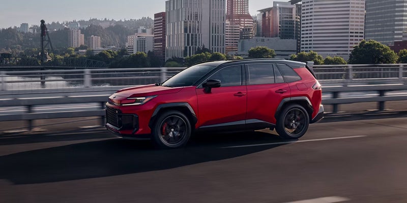 Red Toyota RAV4 SUV driving across a city bridge with buildings in the background.